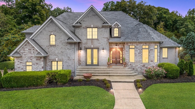 french provincial home featuring roof with shingles, a front yard, and french doors