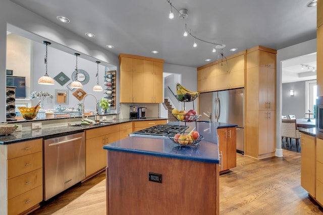 kitchen with a kitchen island, appliances with stainless steel finishes, dark stone countertops, light wood-style floors, and a sink