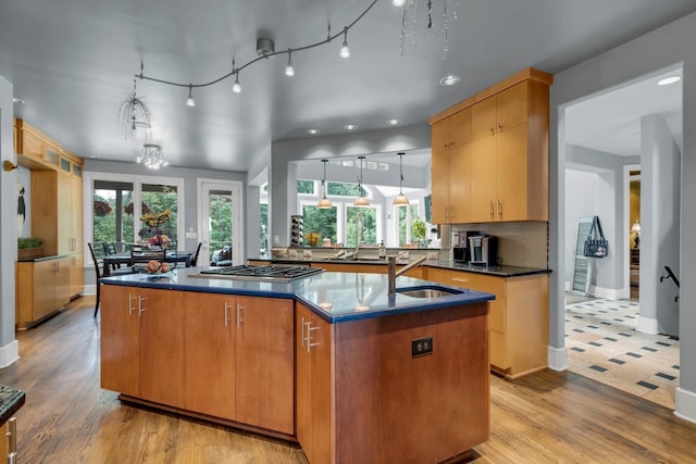 kitchen with a center island with sink, decorative backsplash, decorative light fixtures, stainless steel gas cooktop, and a sink