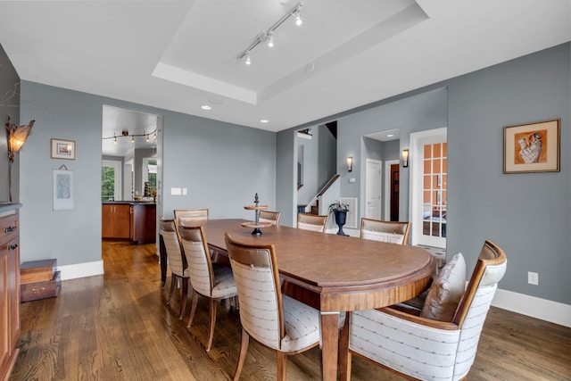 dining area with dark wood-type flooring, a raised ceiling, track lighting, and baseboards