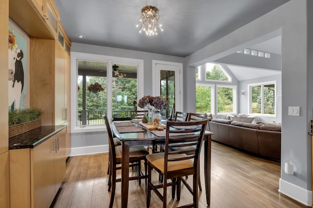 dining space featuring a notable chandelier, light wood finished floors, lofted ceiling, and baseboards