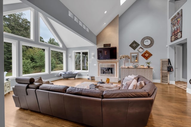 living area featuring light wood-style floors, baseboards, high vaulted ceiling, and a tiled fireplace