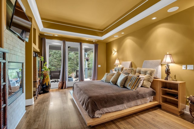 bedroom featuring light wood-type flooring, access to exterior, a raised ceiling, and recessed lighting