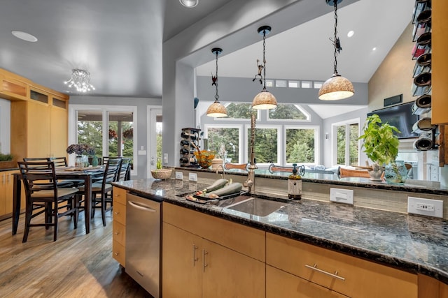 kitchen featuring lofted ceiling, light wood-style flooring, hanging light fixtures, dark stone countertops, and glass insert cabinets