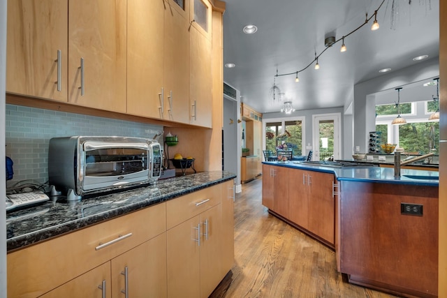 kitchen featuring a toaster, hanging light fixtures, light wood-style flooring, glass insert cabinets, and dark stone countertops