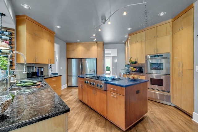 kitchen with a sink, appliances with stainless steel finishes, light wood-type flooring, a center island, and a warming drawer