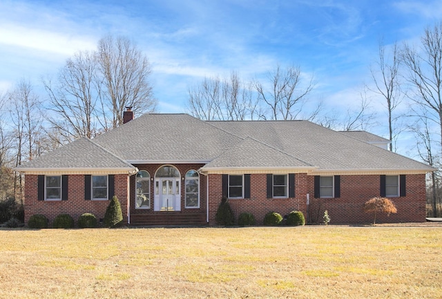 ranch-style house featuring roof with shingles, brick siding, a chimney, and a front lawn