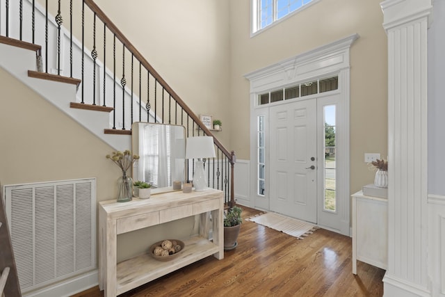 foyer entrance with a wainscoted wall, a high ceiling, wood finished floors, visible vents, and stairs