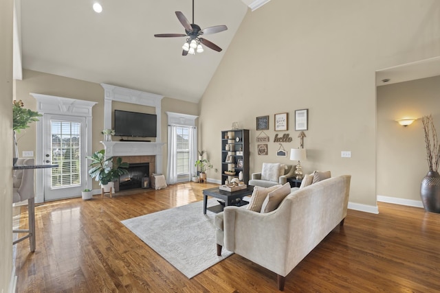 living area featuring baseboards, dark wood finished floors, a tile fireplace, ceiling fan, and high vaulted ceiling