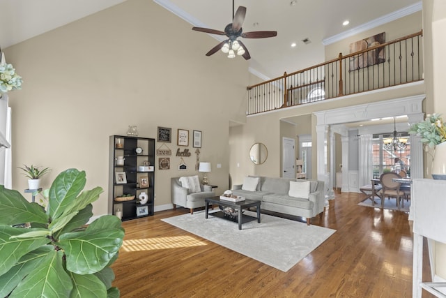 living area with a high ceiling, ornamental molding, wood finished floors, ornate columns, and ceiling fan with notable chandelier