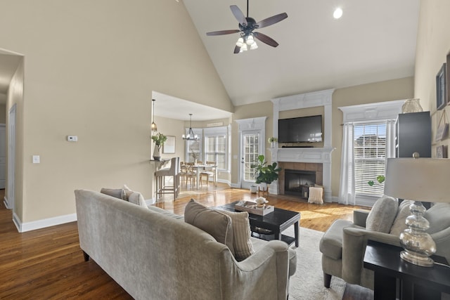 living room with high vaulted ceiling, a fireplace, baseboards, and wood finished floors