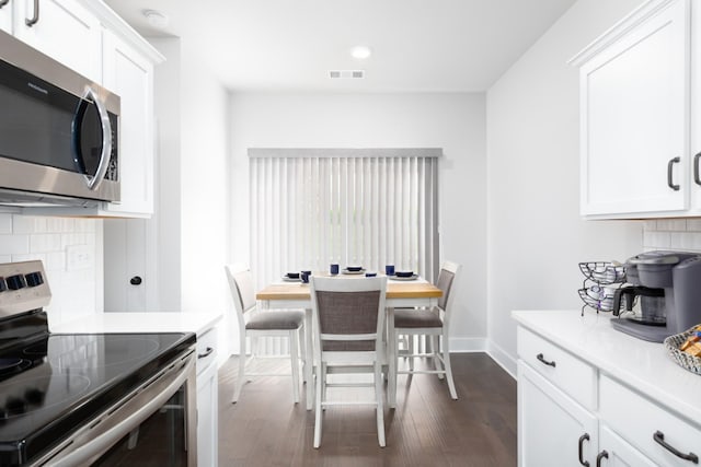 kitchen featuring tasteful backsplash, white cabinets, appliances with stainless steel finishes, dark wood-type flooring, and light countertops