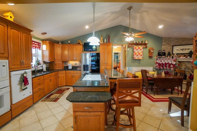 kitchen featuring white appliances, dark countertops, a kitchen island, hanging light fixtures, and light tile patterned flooring