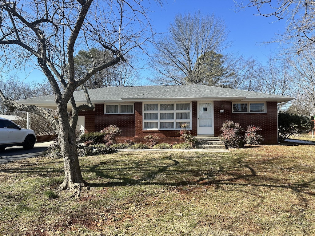 single story home with a front lawn, an attached carport, and brick siding