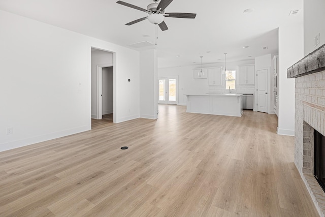 unfurnished living room featuring visible vents, light wood-type flooring, a brick fireplace, and a ceiling fan