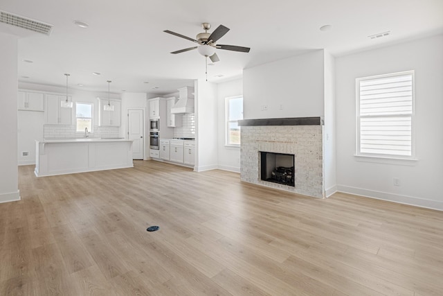 unfurnished living room with light wood-style flooring, a fireplace, visible vents, and ceiling fan