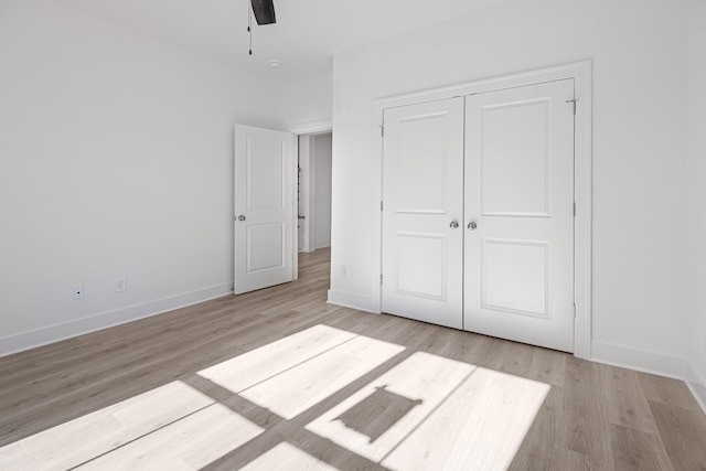 unfurnished bedroom with light wood finished floors, a closet, a ceiling fan, and baseboards