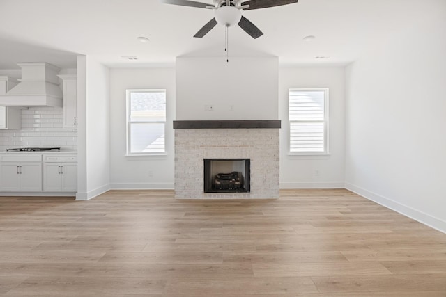 unfurnished living room featuring baseboards, ceiling fan, a fireplace, and light wood-style floors