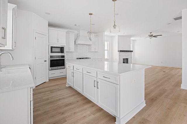 kitchen with white cabinets, oven, built in microwave, premium range hood, and a sink