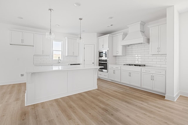 kitchen featuring light wood finished floors, light countertops, custom range hood, appliances with stainless steel finishes, and white cabinets