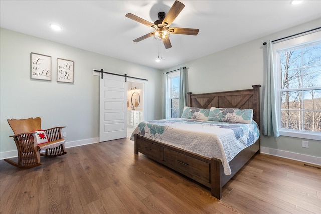 bedroom with a barn door, wood finished floors, visible vents, and baseboards