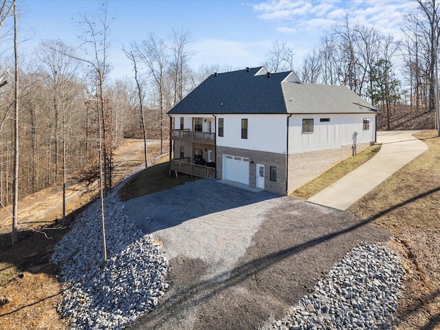 view of side of home with driveway, a balcony, an attached garage, and a shingled roof