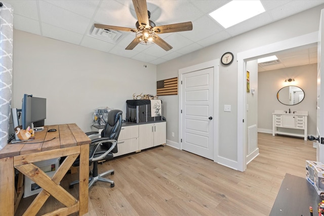 office with a drop ceiling, light wood-type flooring, visible vents, and a ceiling fan