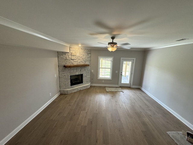 unfurnished living room with a stone fireplace, a ceiling fan, visible vents, baseboards, and dark wood finished floors