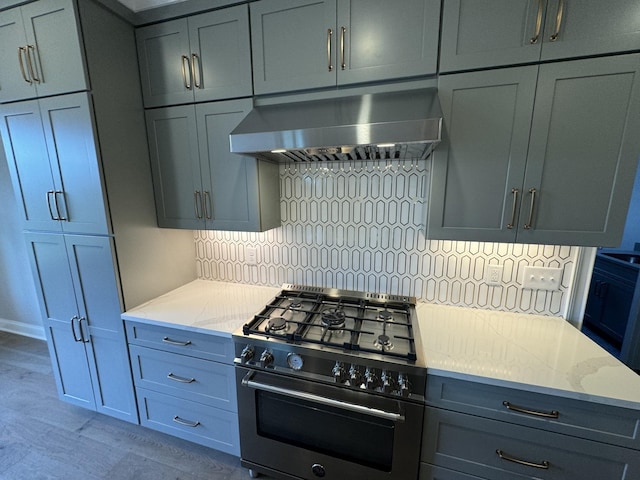 kitchen featuring exhaust hood, high end stainless steel range, backsplash, light stone countertops, and light wood finished floors