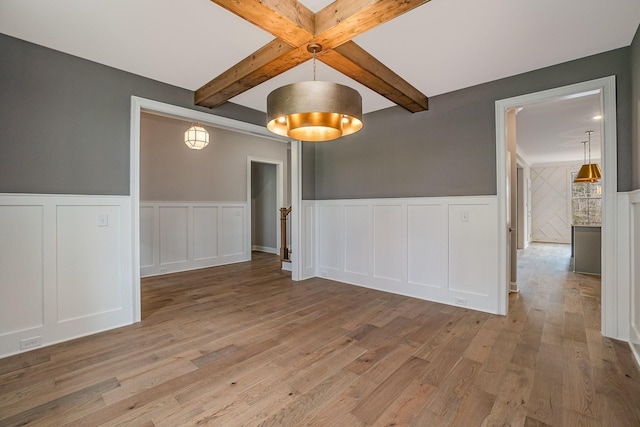 spare room featuring light wood finished floors, beamed ceiling, and wainscoting