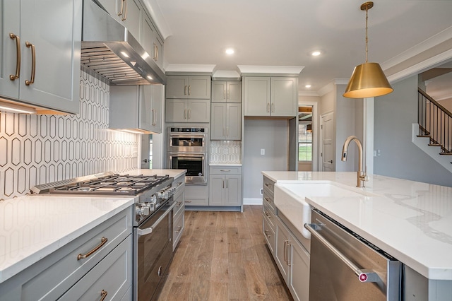 kitchen featuring appliances with stainless steel finishes, light stone counters, crown molding, pendant lighting, and exhaust hood