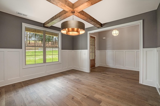 unfurnished room with a wainscoted wall, visible vents, dark wood-style flooring, and beam ceiling