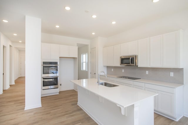 kitchen with tasteful backsplash, white cabinets, an island with sink, stainless steel appliances, and a sink