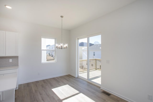 unfurnished dining area featuring a healthy amount of sunlight, light wood-type flooring, visible vents, and a notable chandelier