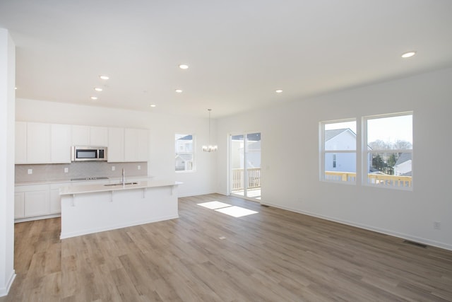 kitchen with a sink, visible vents, light countertops, decorative backsplash, and stainless steel microwave