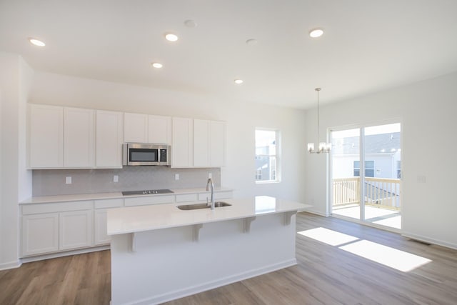 kitchen featuring stainless steel microwave, a sink, black electric stovetop, white cabinetry, and backsplash