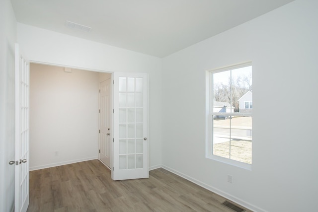 unfurnished room with a wealth of natural light, visible vents, baseboards, and wood finished floors