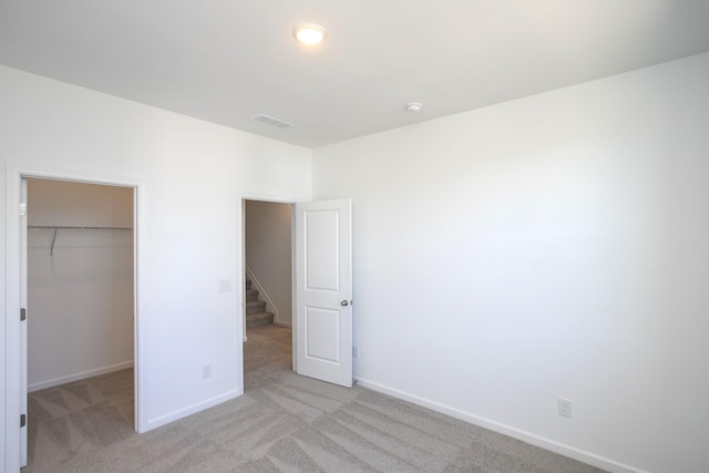 unfurnished bedroom with baseboards, visible vents, a walk in closet, and light colored carpet