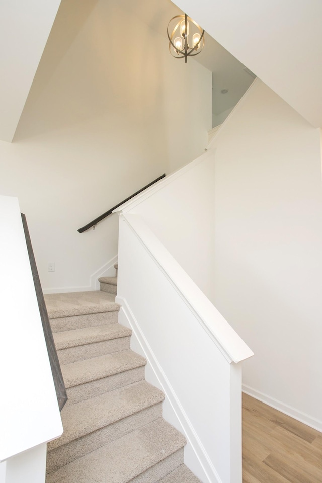 staircase featuring baseboards, a chandelier, and wood finished floors