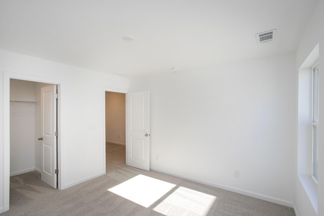 unfurnished bedroom with baseboards, visible vents, a walk in closet, and light colored carpet