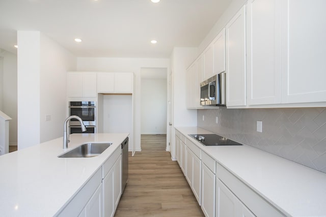 kitchen featuring stainless steel appliances, white cabinetry, a sink, and decorative backsplash