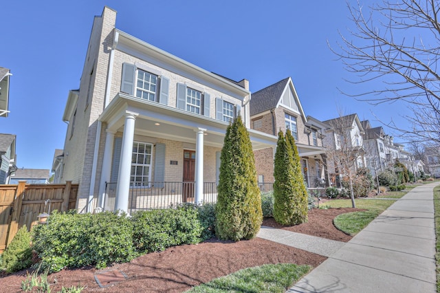 view of front of home featuring brick siding, a chimney, a porch, fence, and a residential view