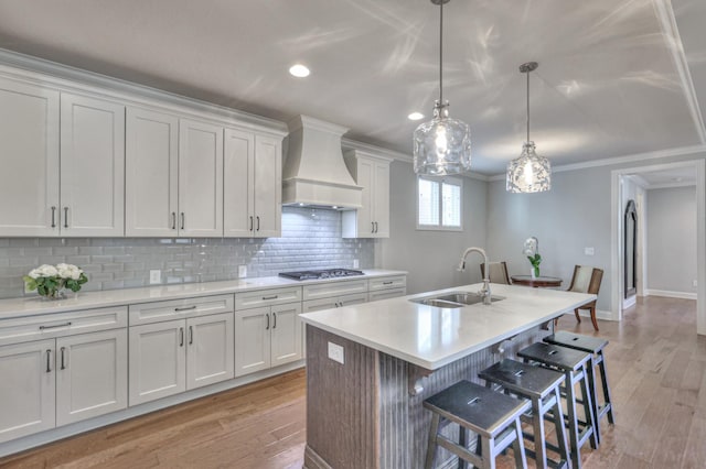 kitchen featuring crown molding, light countertops, decorative backsplash, a sink, and premium range hood