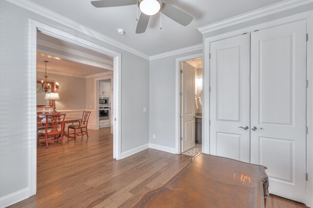 interior space with ceiling fan with notable chandelier, wood finished floors, baseboards, a closet, and crown molding