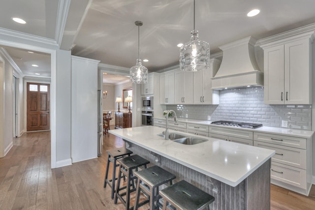 kitchen with a sink, light countertops, appliances with stainless steel finishes, and custom exhaust hood