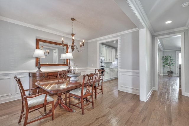 dining room featuring a wainscoted wall, ornamental molding, a decorative wall, and light wood-style floors