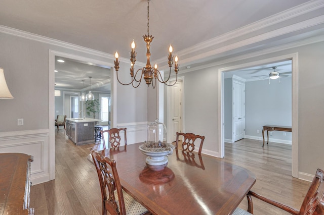 dining space with crown molding, light wood-style flooring, a decorative wall, and ceiling fan with notable chandelier