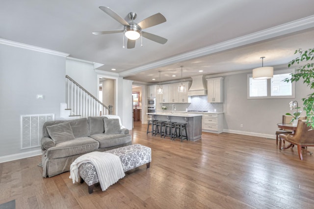 living room with light wood finished floors, baseboards, visible vents, stairs, and crown molding