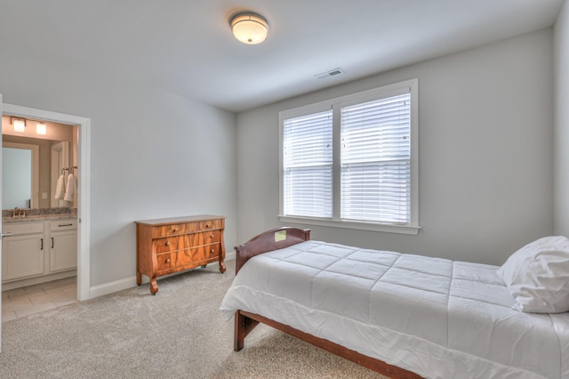 bedroom featuring visible vents, ensuite bathroom, light carpet, a sink, and baseboards