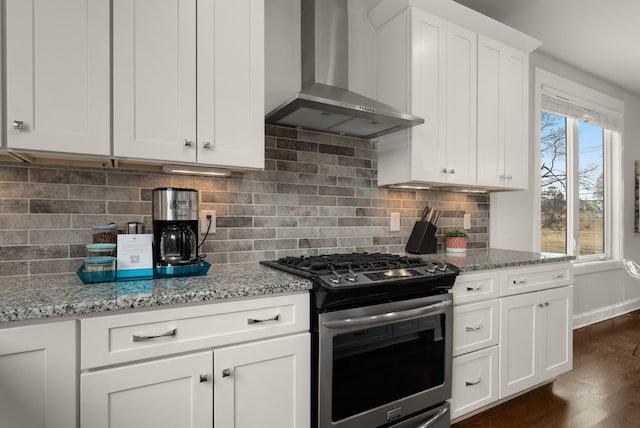 kitchen featuring stainless steel gas range oven, white cabinets, light stone countertops, wall chimney exhaust hood, and tasteful backsplash